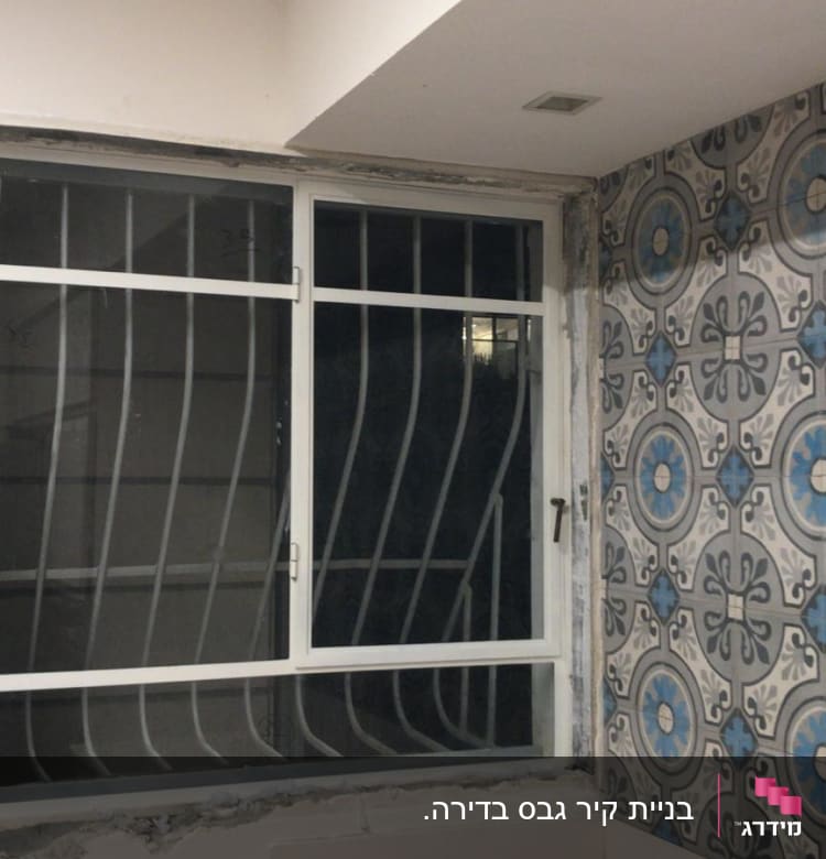 חלון עם מסגרת מתכת וקיר עם אריחים מעוצבים